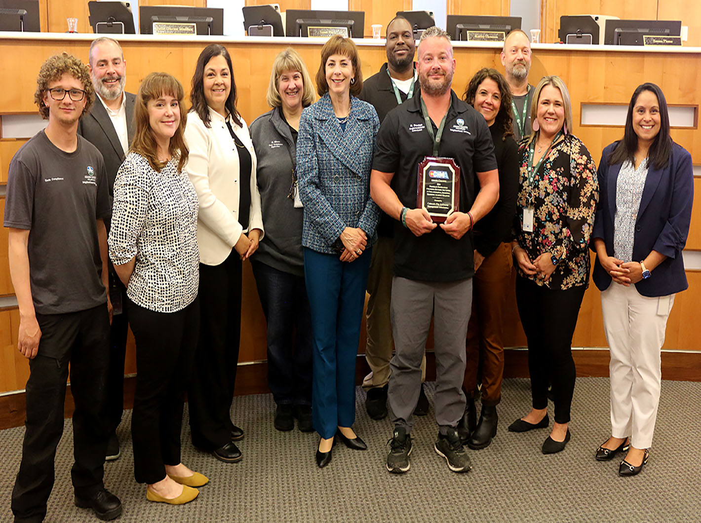 A group of twelve people in business attire smiling, one holding an award plaque.