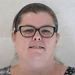 Person with glasses and headband, smiling, against plain background.