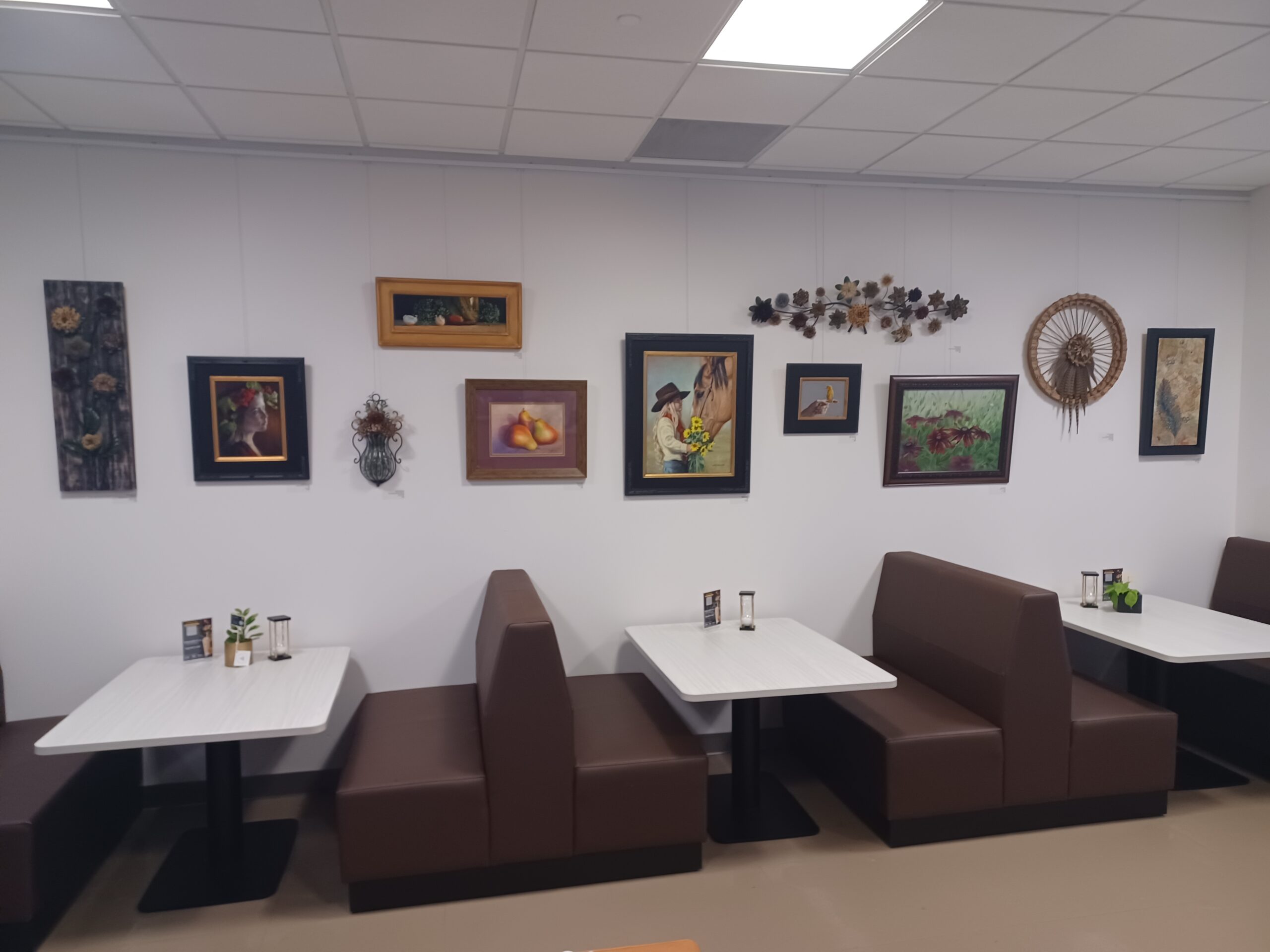 Art-filled café wall with brown booths and white tables.