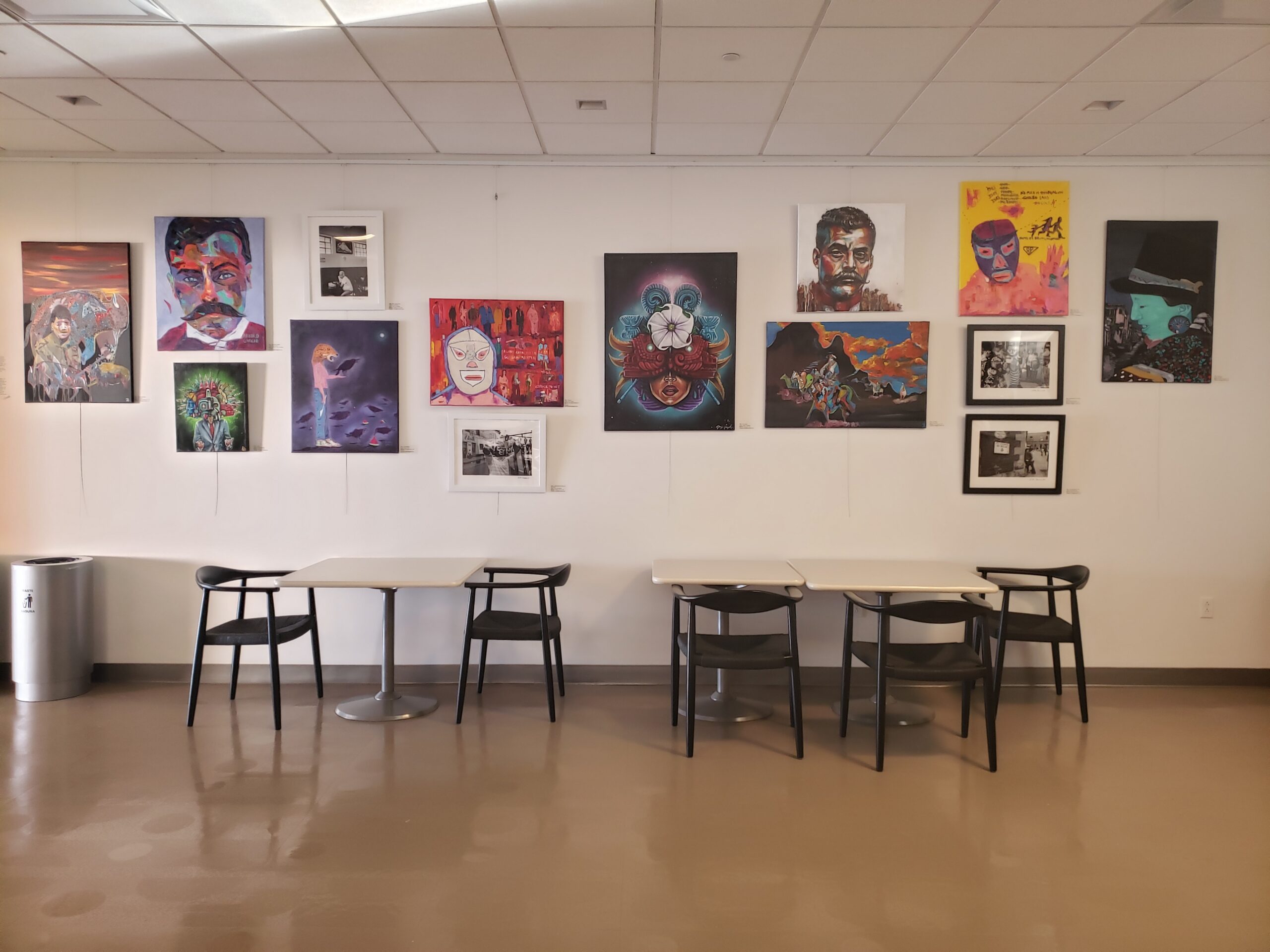 Art gallery wall featuring colorful paintings and photographs above dining tables and chairs.