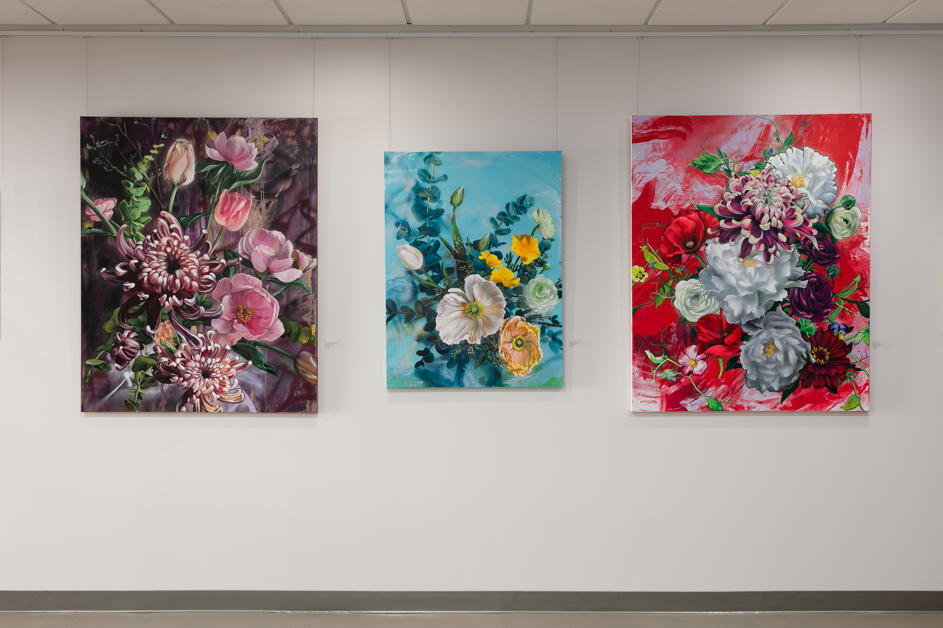Three vibrant floral paintings on a gallery wall, each with different backgrounds and arrangements.