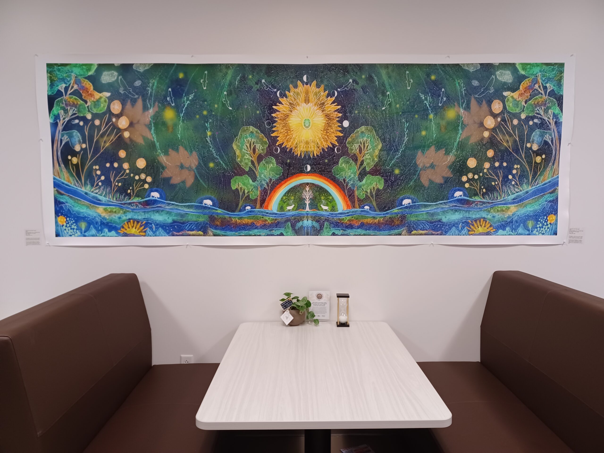 Colorful cosmic-themed mural with sun, trees, and rainbow above a seating area.
