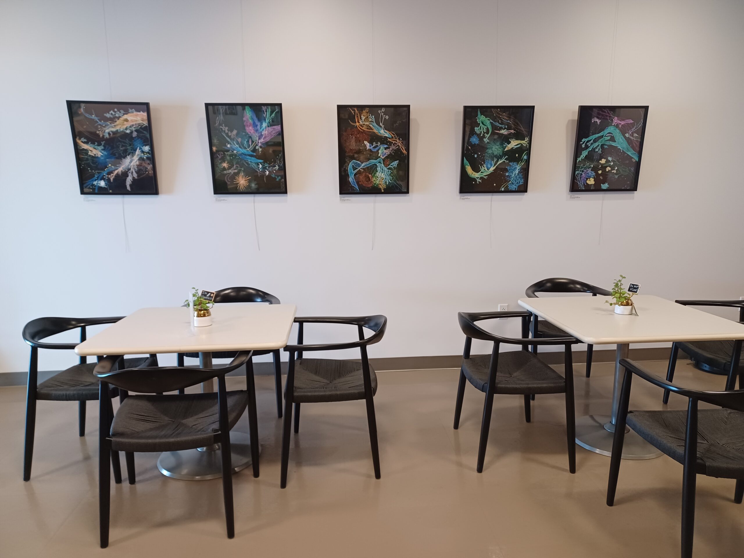 Artistic cafe setting with abstract paintings on wall, tables and chairs below.