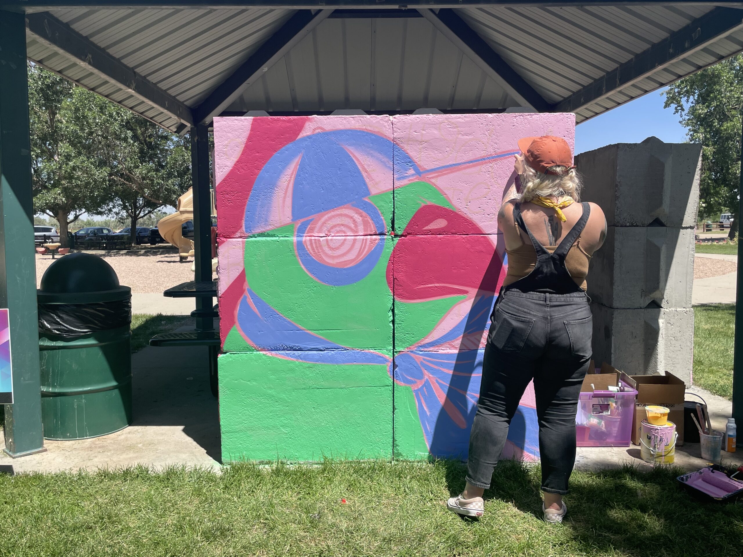 Person painting colorful mural in park pavilion.