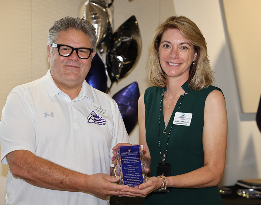 Man and woman smiling, holding an award plaque together