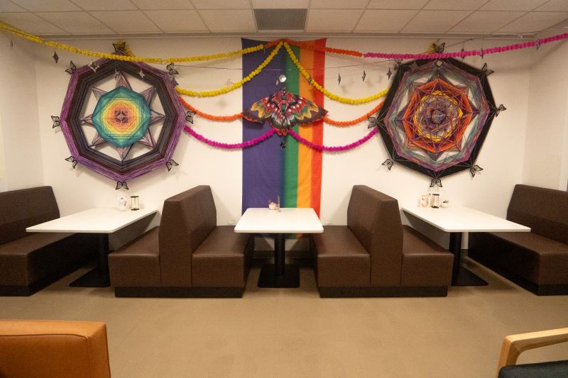 Colorful wall decorations with geometric designs and Pride flag in a cozy booth seating area.