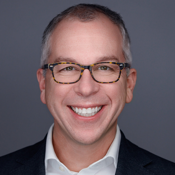 Jason Schultz smiling, wearing glasses and a suit with a white shirt