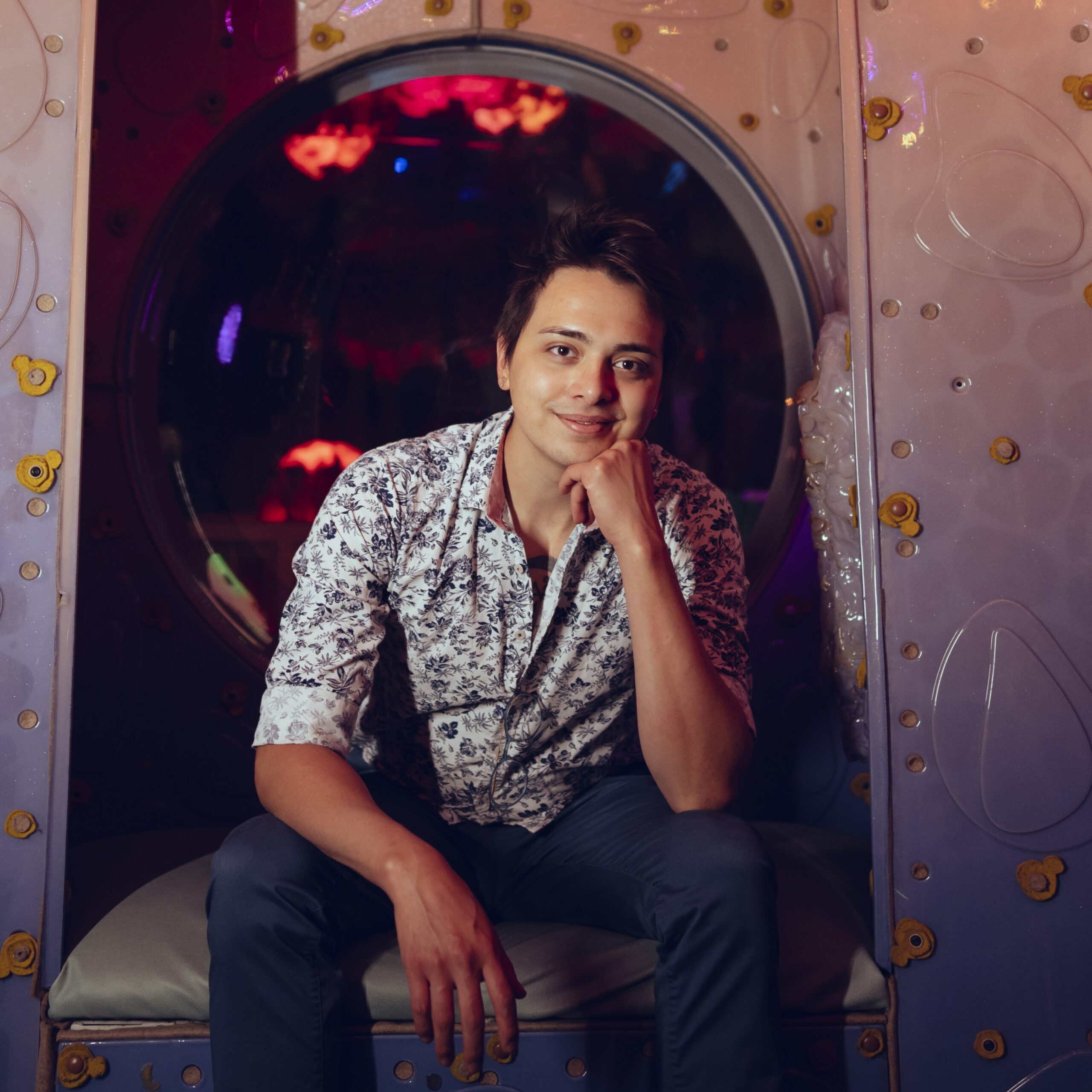 Brandon Vargas sitting in a whimsical, colorful setting, smiling at the camera.