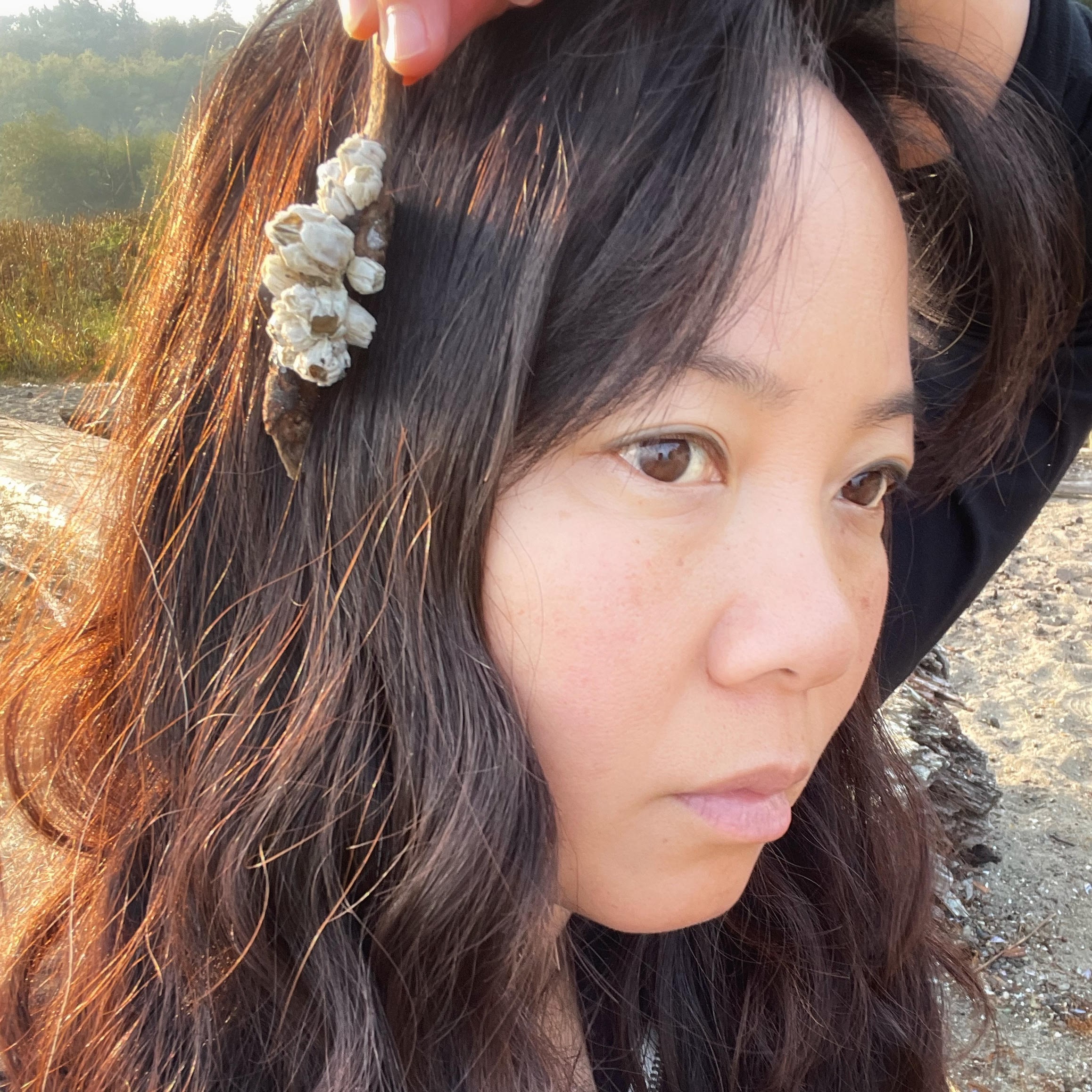 Christine holding seashell hair accessory, outdoors in natural light