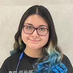 Dominique smiling, wearing glasses, with long hair transitioning from dark to light blue at the ends