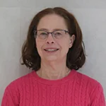 Elisa smiling, wearing glasses and a pink sweater, against a neutral background.