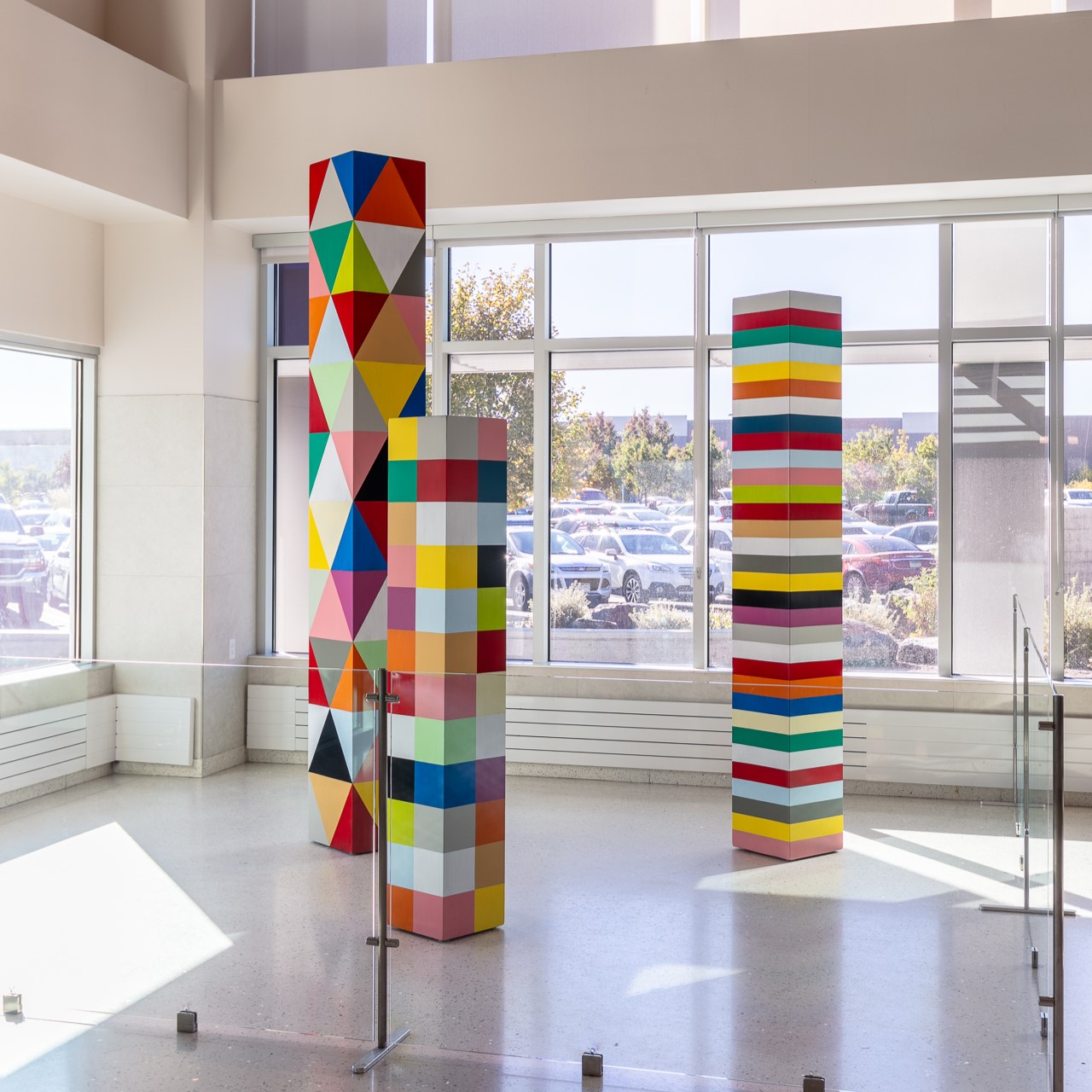 Colorful geometric sculptures with triangles and squares in a sunlit gallery space.