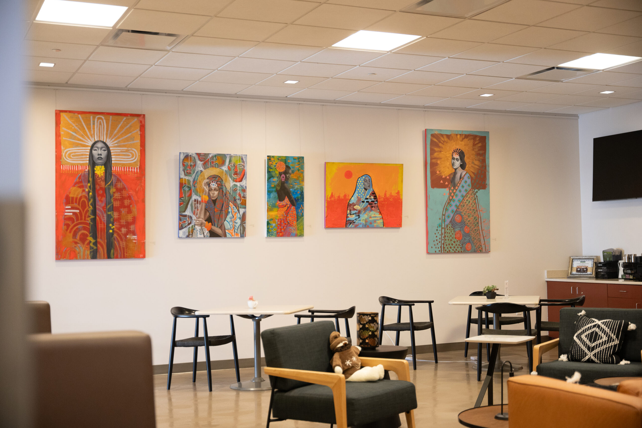 Colorful artwork featuring diverse cultural portraits displayed in a modern lounge setting.