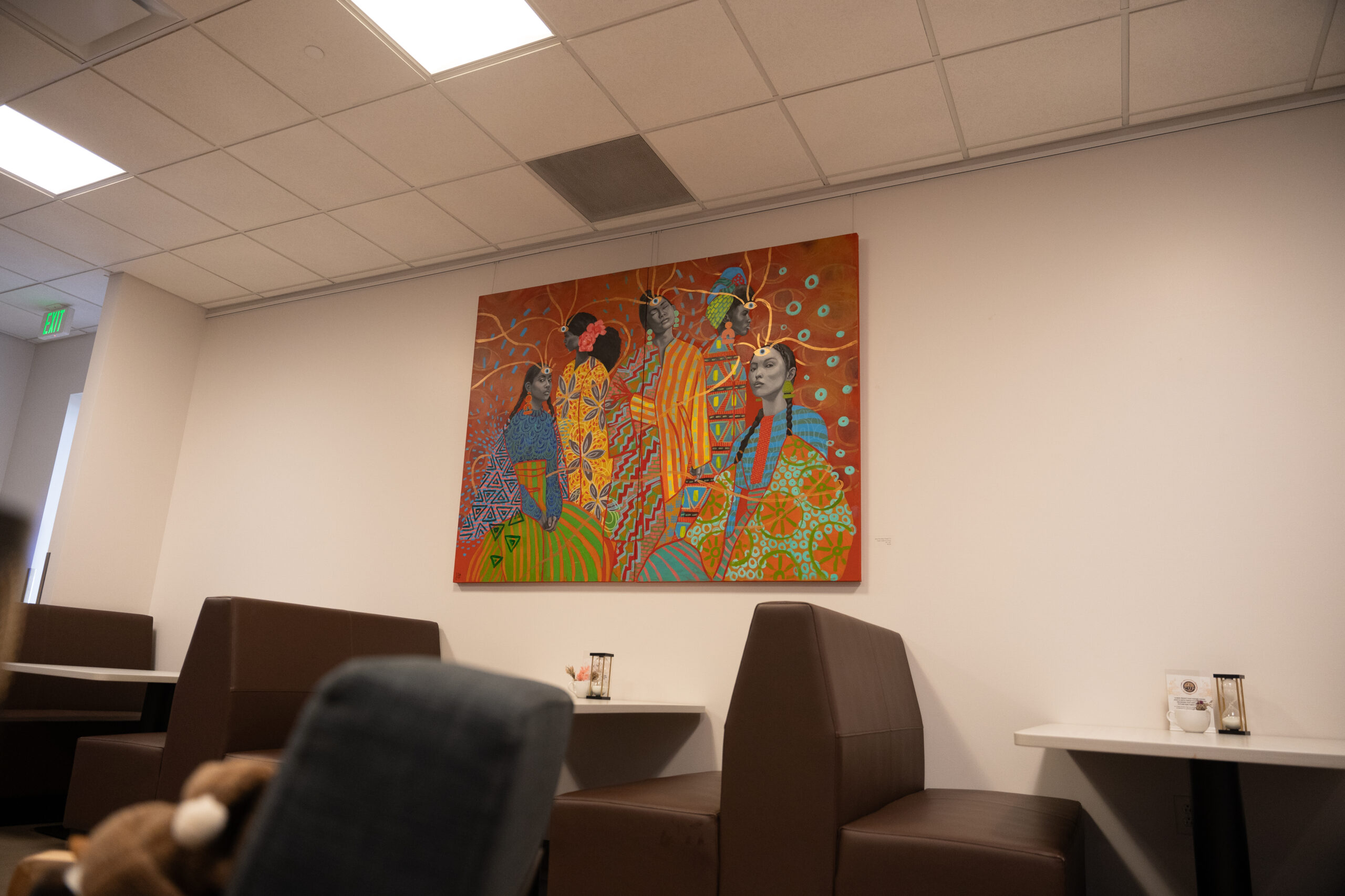 Colorful mural with abstract figures on cafeteria wall, brown booths beneath