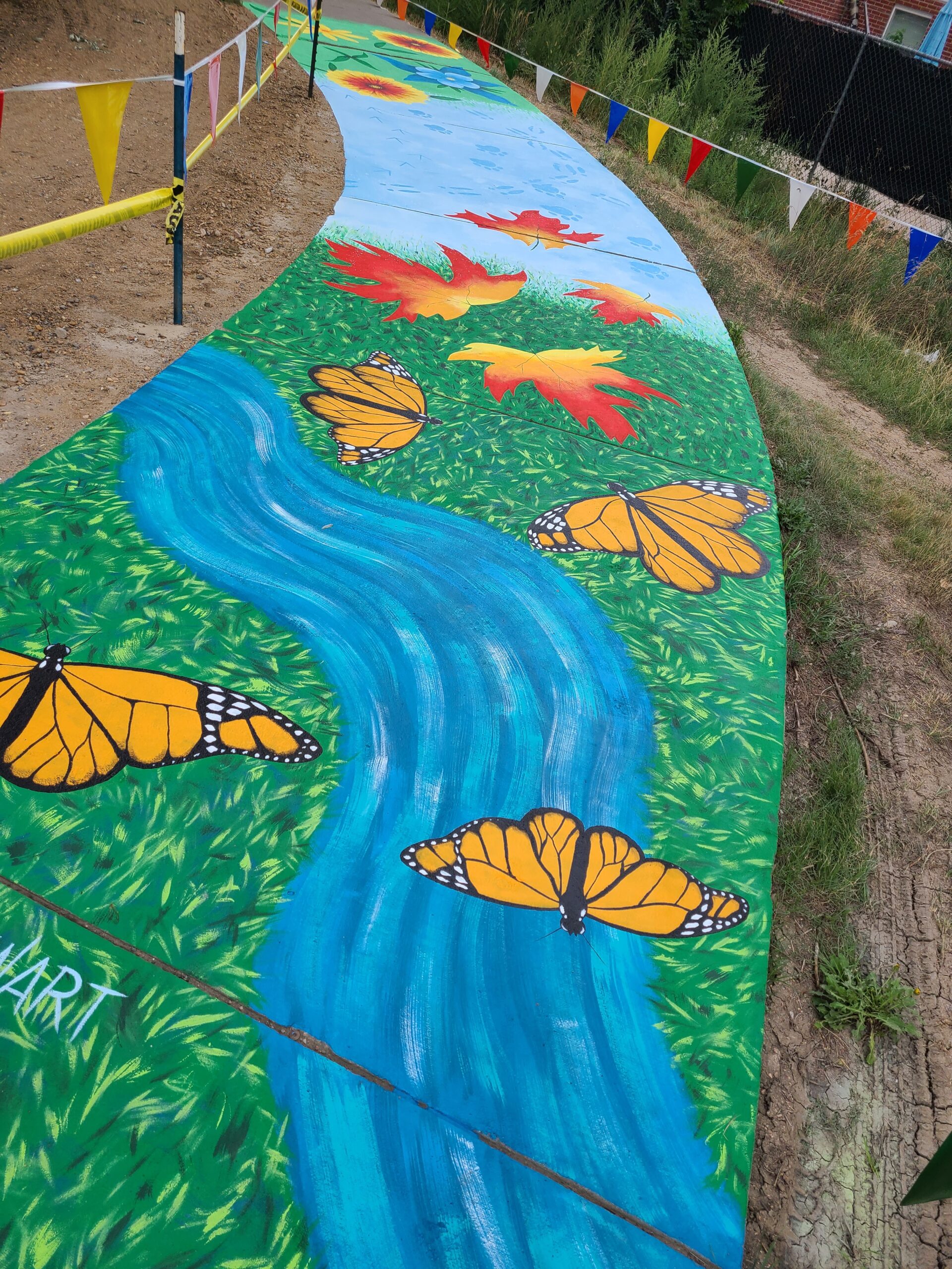 Colorful pathway mural with monarch butterflies, autumn leaves, and a winding blue stream.