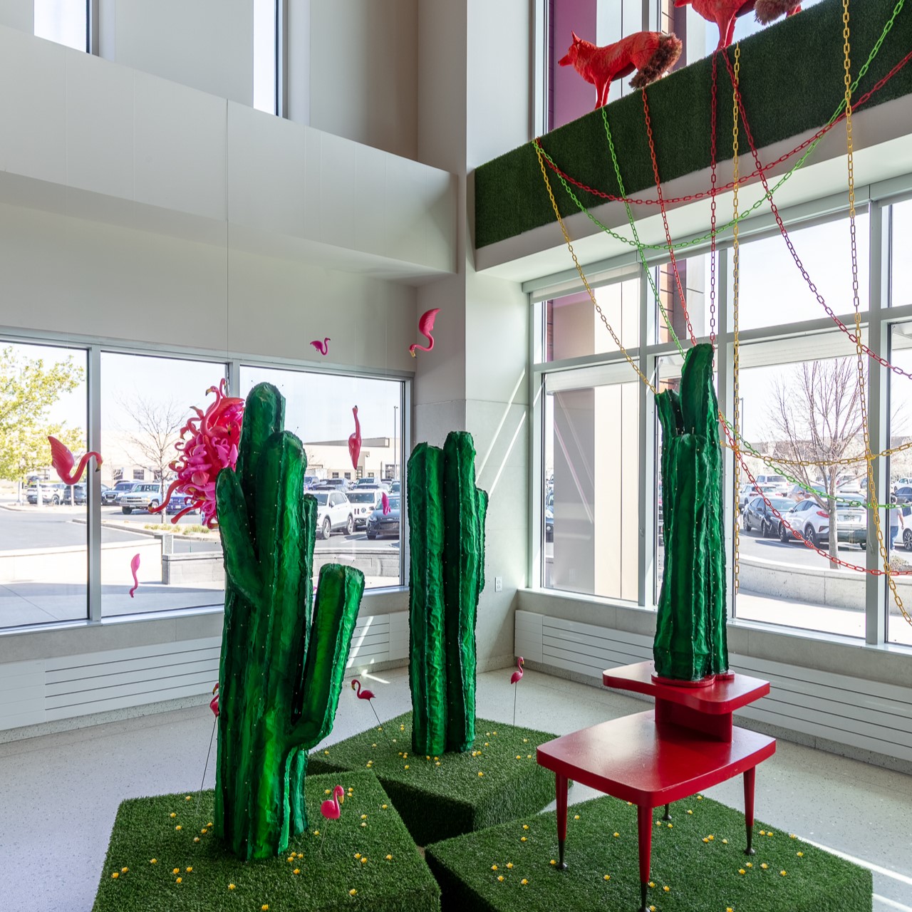 Bright indoor installation with green cacti, pink flamingos, colorful chains, and red fox figurines.