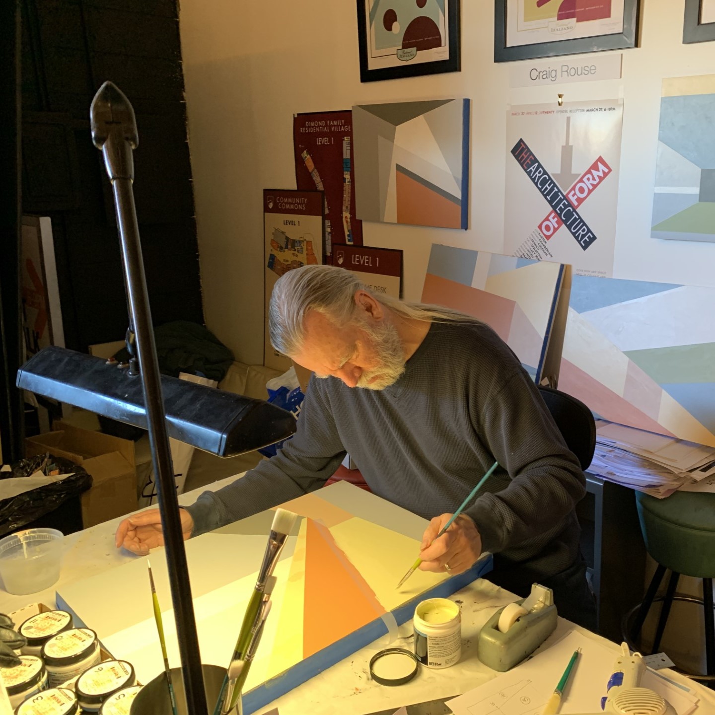 MicrosoftTeams-image-1.jpg: Artist painting in studio, surrounded by geometric artworks and supplies.