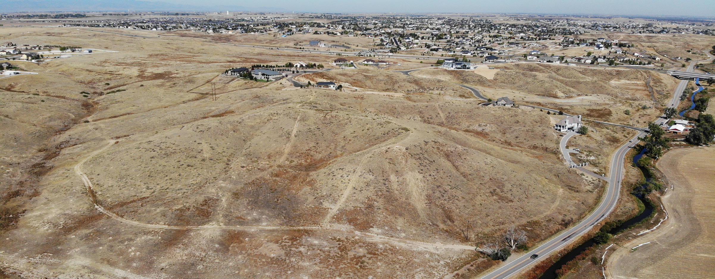 Aerial view of Riverdale Bluffs, showing brown hills with sparse vegetation, houses, and winding roads in a residential area.