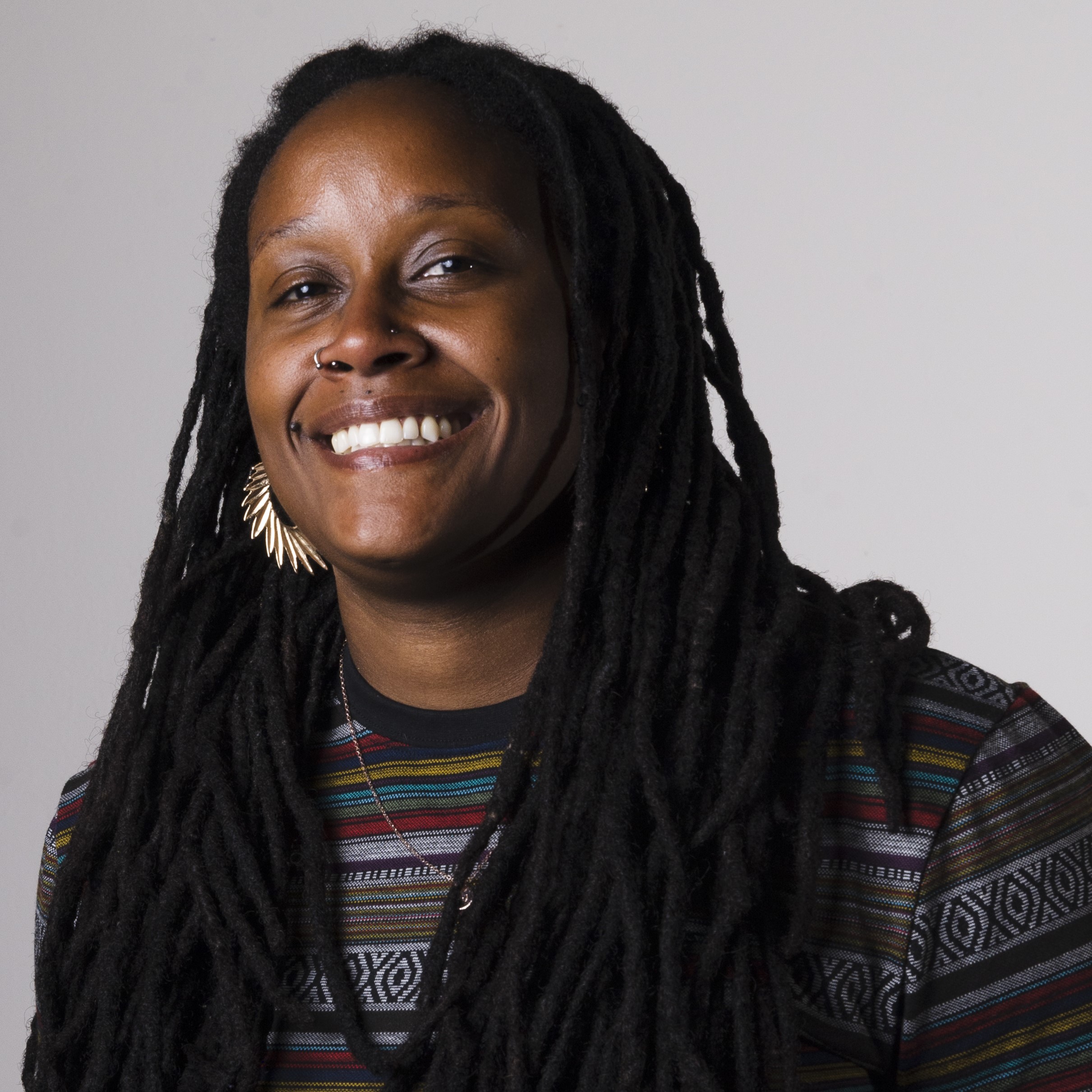 Shaunie smiling, wearing patterned top and leaf-shaped earrings