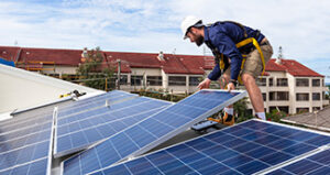 Worker in safety gear installing solar panels on a rooftop