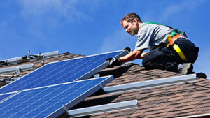 A person installing solar panels on a roof under a clear blue sky.