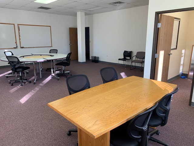 Conference room with wooden table, black chairs, and whiteboards on walls