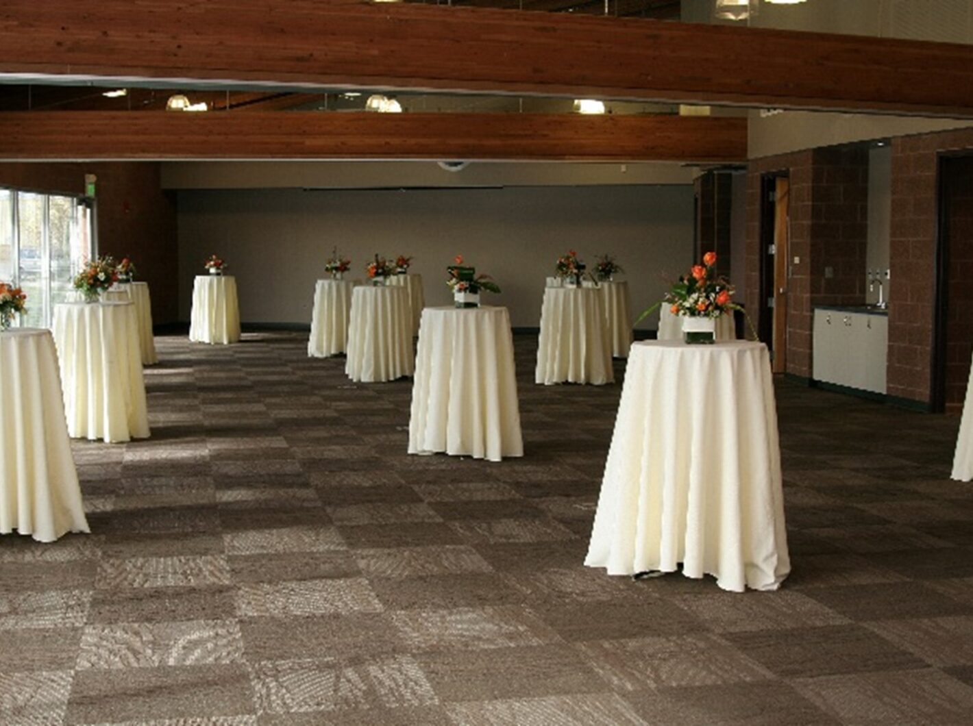 Large room with high tables covered in white cloths, arranged for an event.