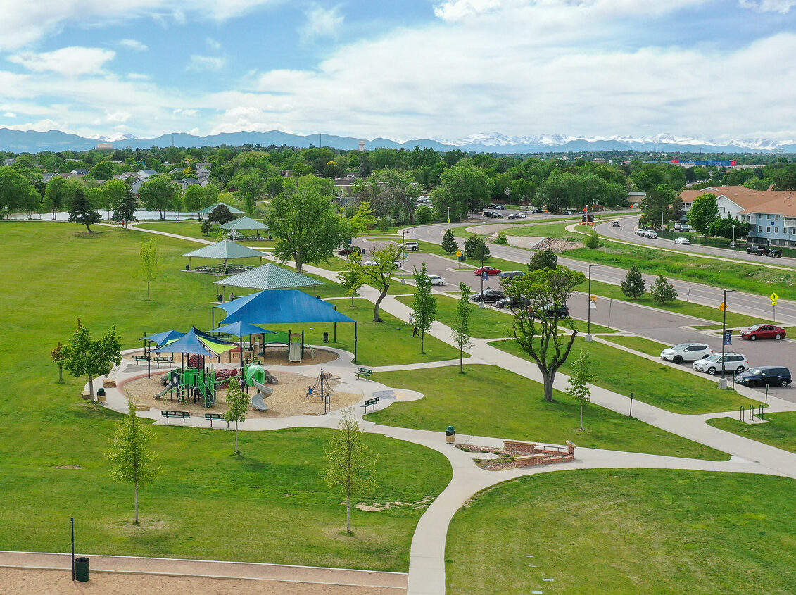 Playground with blue canopies in a park, surrounded by greenery and pathways, mountains visible in the distance