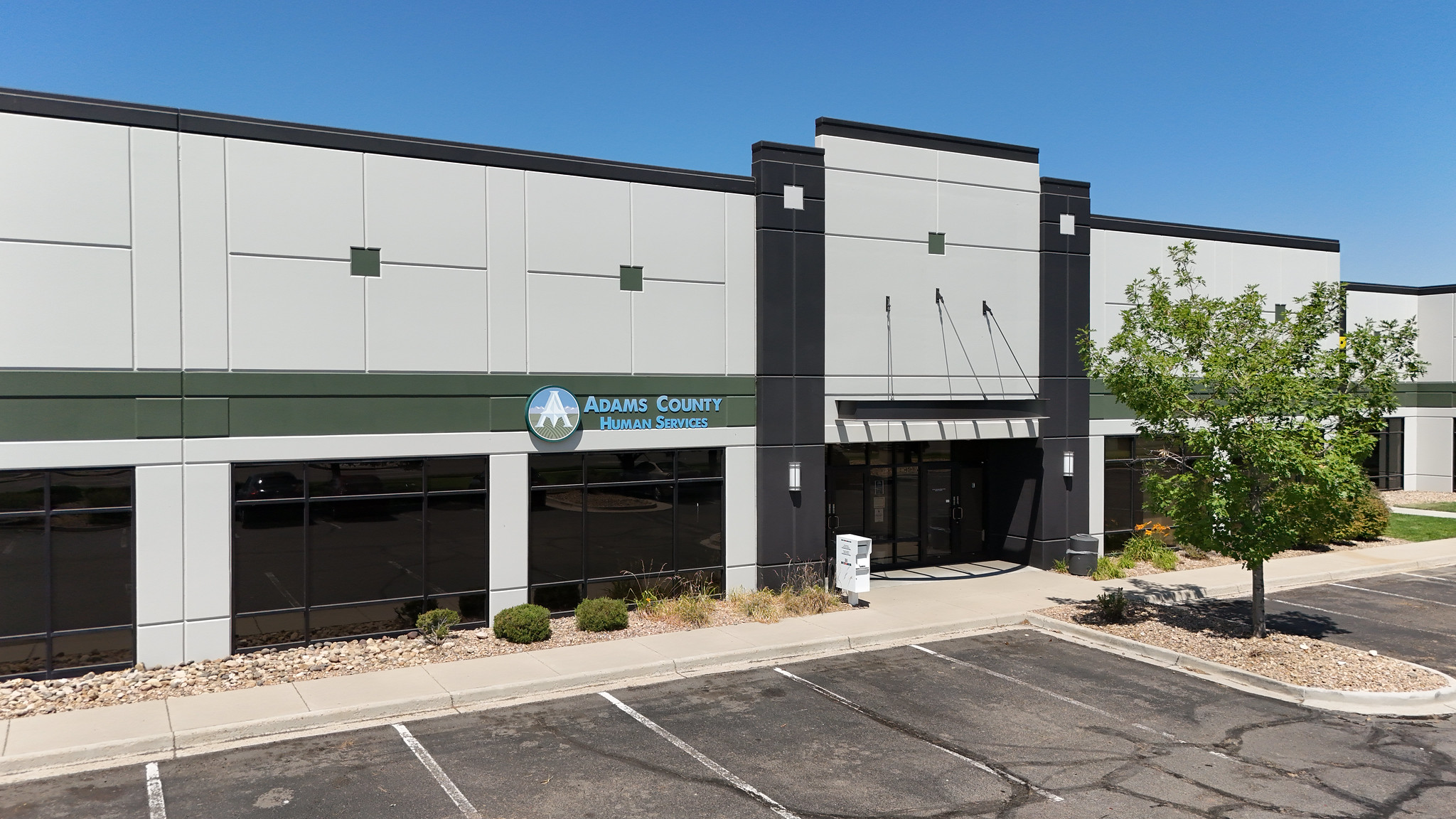 Adams County Human Services building exterior with parking lot and tree