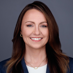 Nicci smiling, wearing a blazer and necklace, against a gray background.
