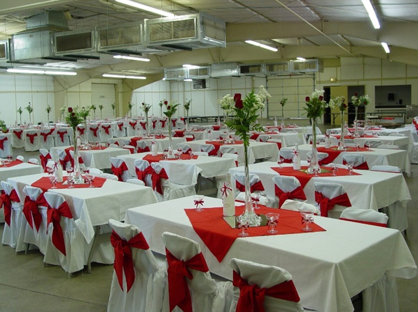 Banquet hall with tables adorned in white and red linens, floral centerpieces, and red bows on chairs