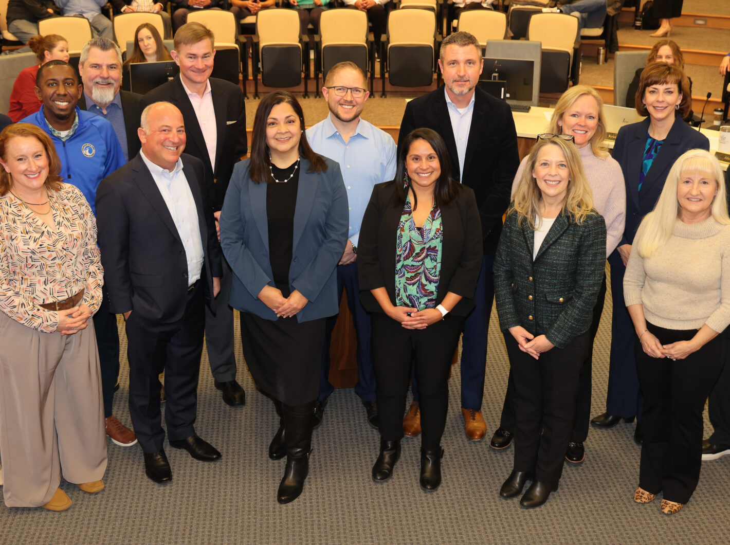 Group of thirteen people smiling, standing in a conference room.