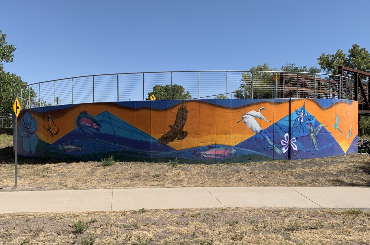 Colorful mural on a curved wall featuring birds, fish, and flowers under a clear blue sky.