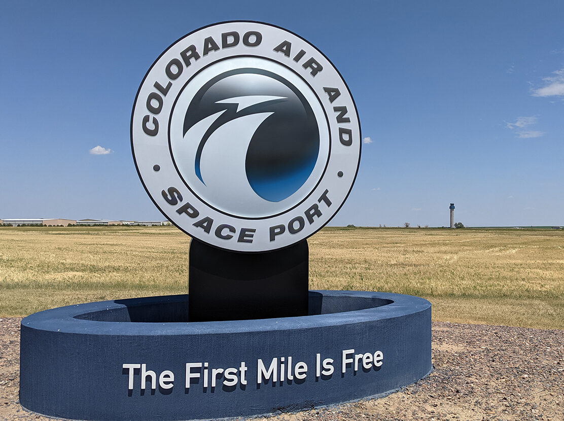 Colorado Air and Space Port sign with text "The First Mile Is Free" in open field.