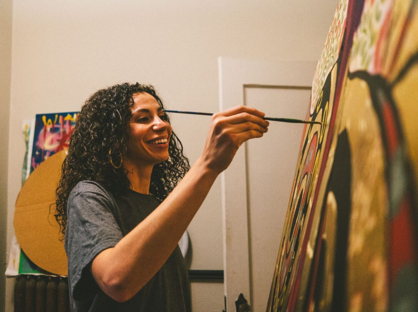 Person joyfully painting vibrant artwork on canvas indoors.