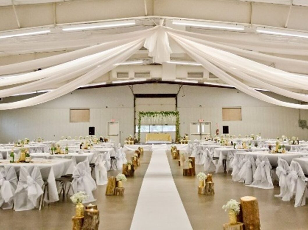 Decorated exhibition hall with white drapes and tables, floral aisle.