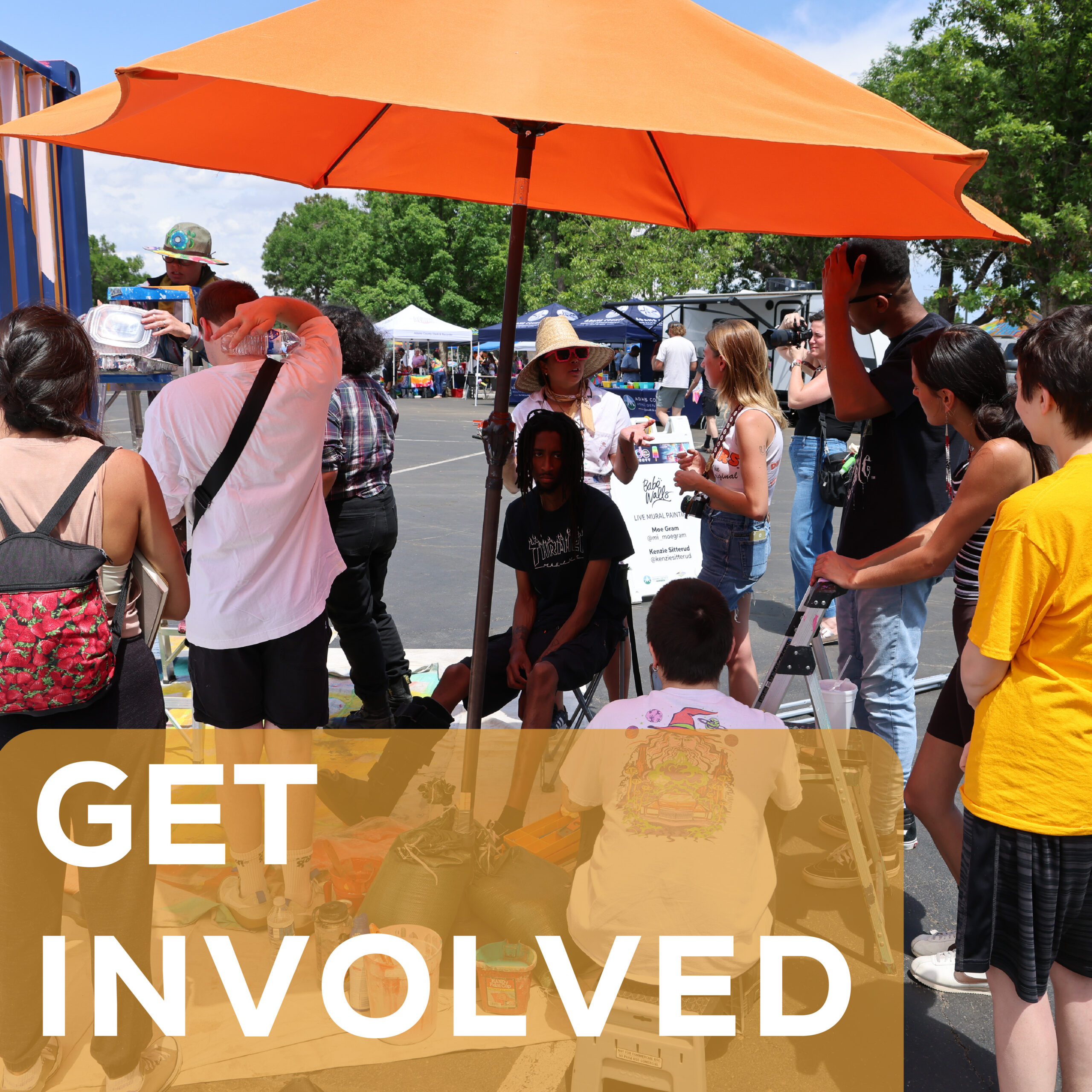 Group of people gathered under an orange umbrella at outdoor event. Text reads "GET INVOLVED."