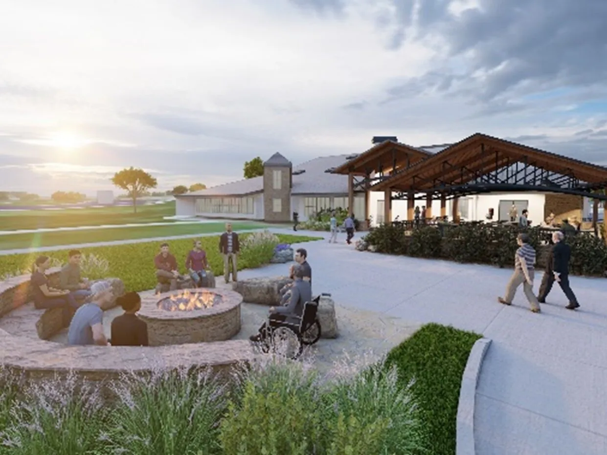 People gather around a fire pit near a modern building at sunset.