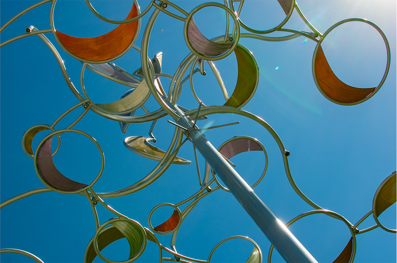 Colorful kinetic sculpture of circular metal shapes against blue sky