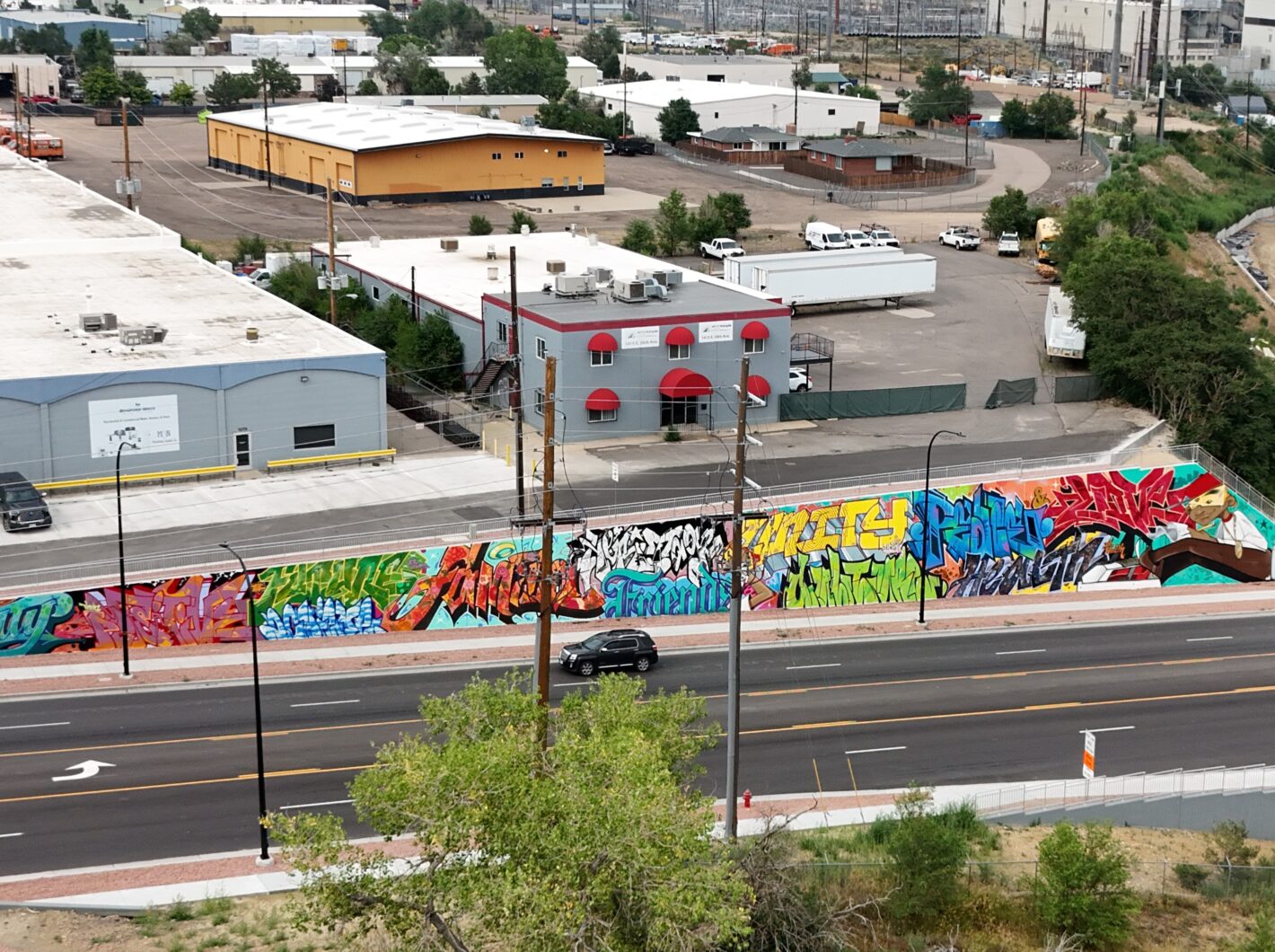 Elevated view of vibrant graffiti mural alongside industrial buildings and parking lot.