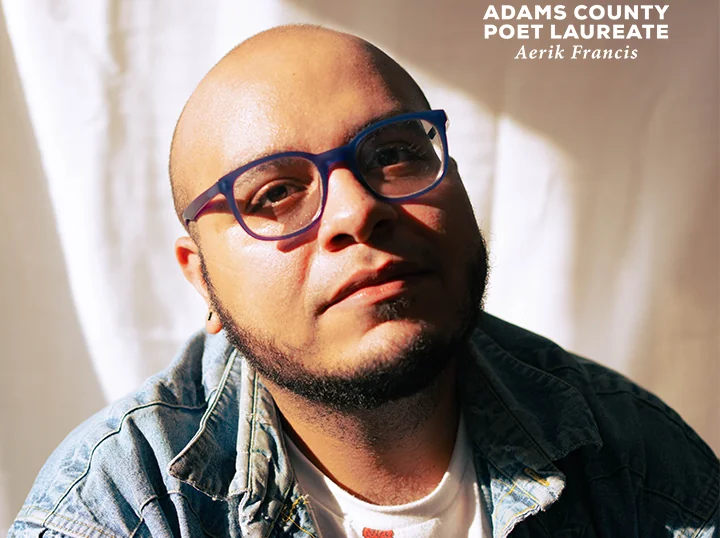 Aerik Francis, wearing glasses and a denim jacket, lit by sunlight. "Adams County Poet Laureate, Aerik Francis" text at top right.