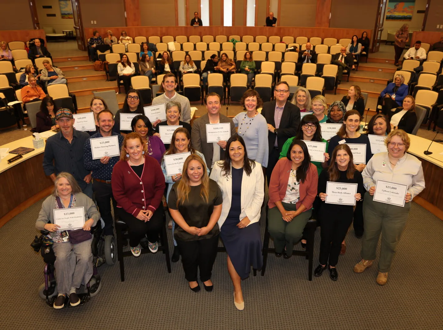 Group of awardees holding certificates in a conference hall, smiling for the camera.
