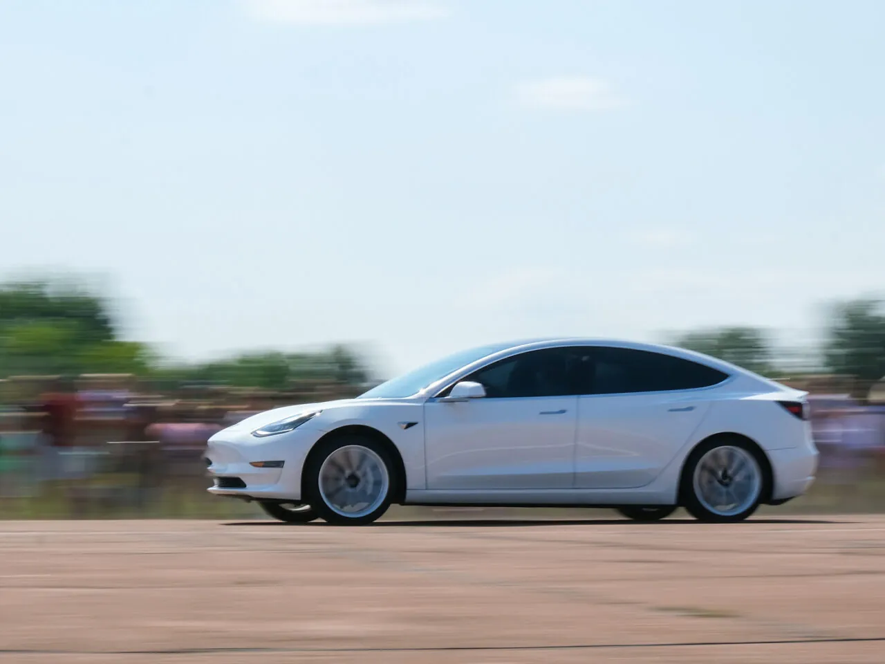 White Tesla Model 3 speeding on a track with blurred spectators.
