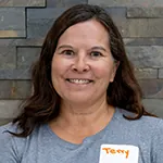 Terry smiling with name tag, standing against stone wall