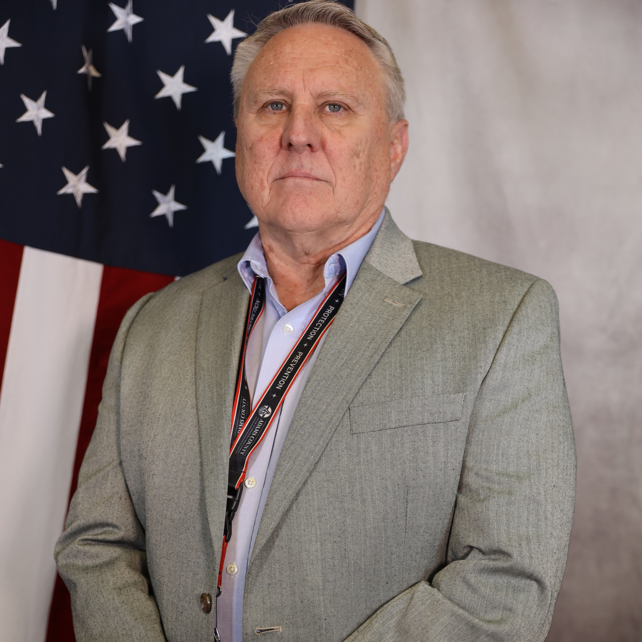 Ronald Sigman in a gray suit stands solemnly before an American flag