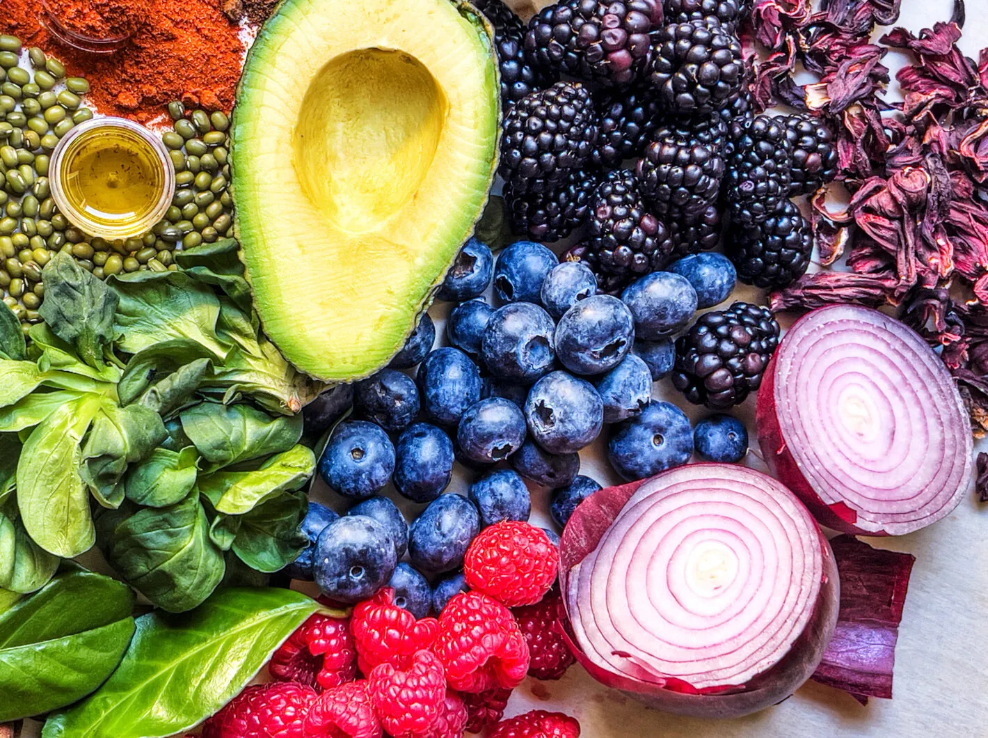 Variety of colorful fruits and vegetables including avocado, blueberries, raspberries, onions, and greens.