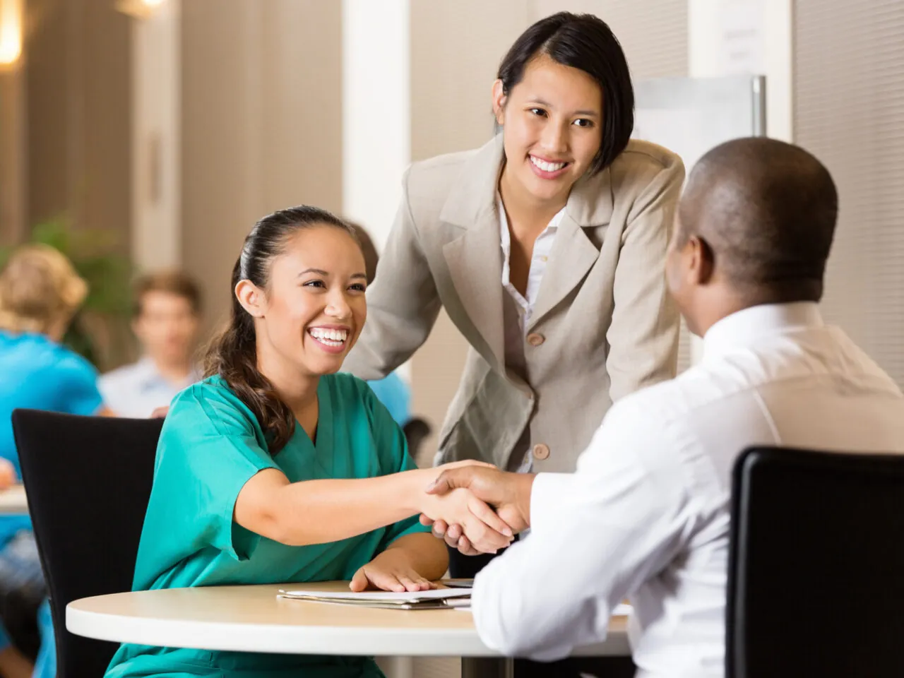 Two women smiling while shaking hands with a seated man