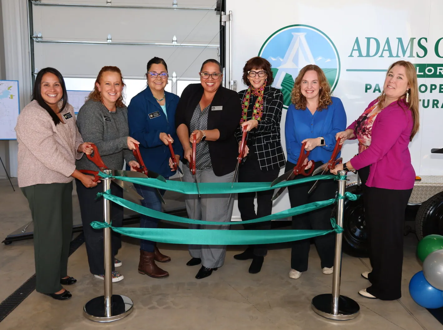 Group of women cutting ribbon at South Parks Operations Building ceremony. Adams County Parks and Open Space backdrop.
