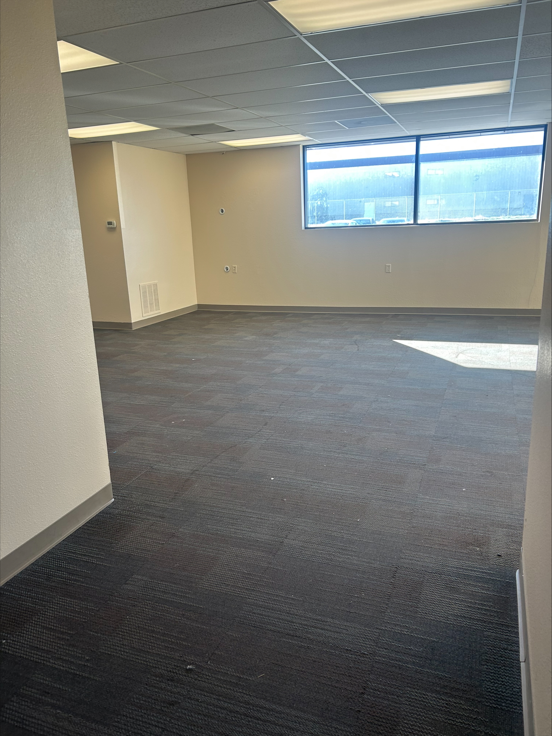 Empty office space with gray carpet, white walls, and large window.