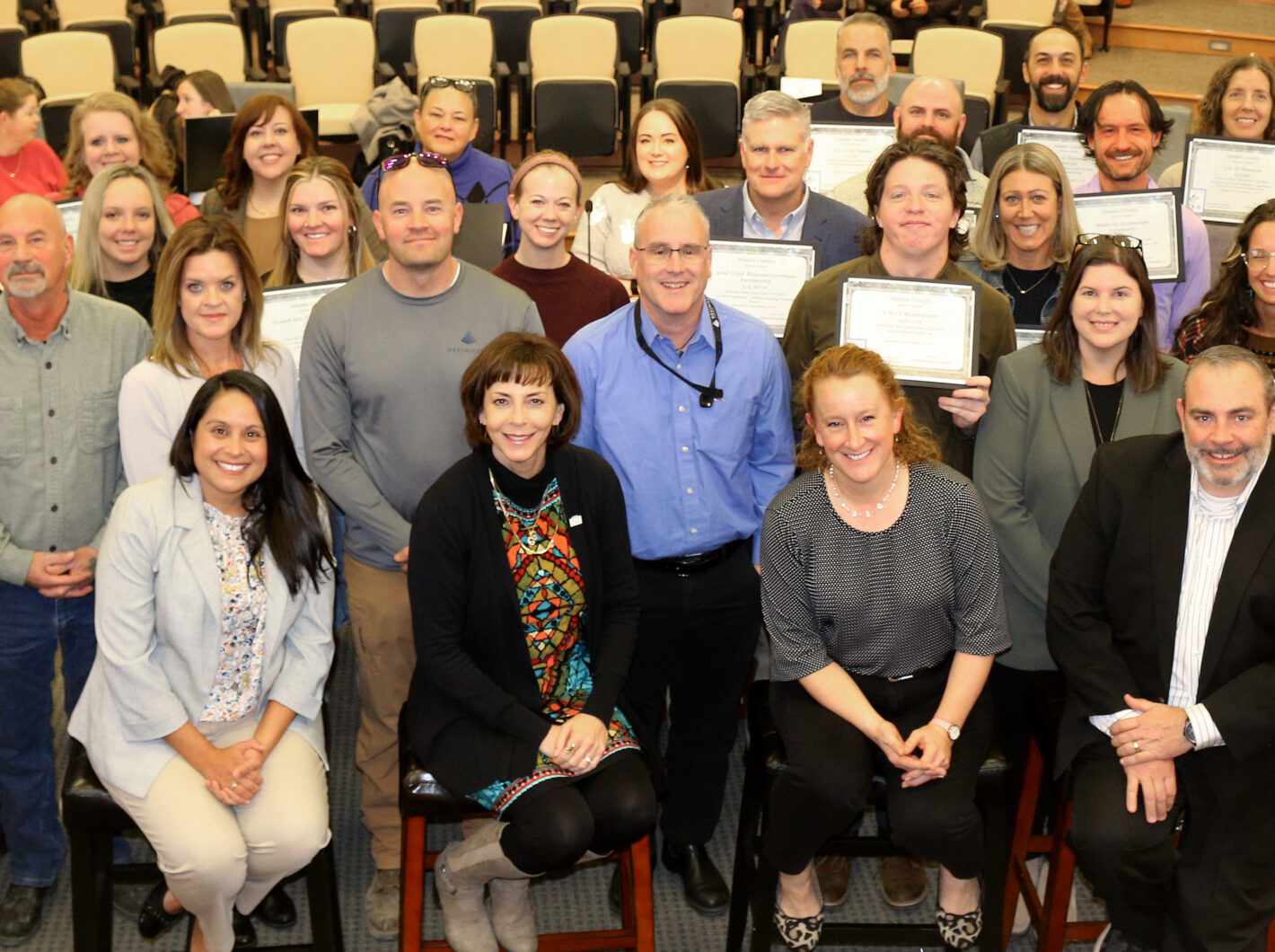 Group of people posing with certificates in an auditorium